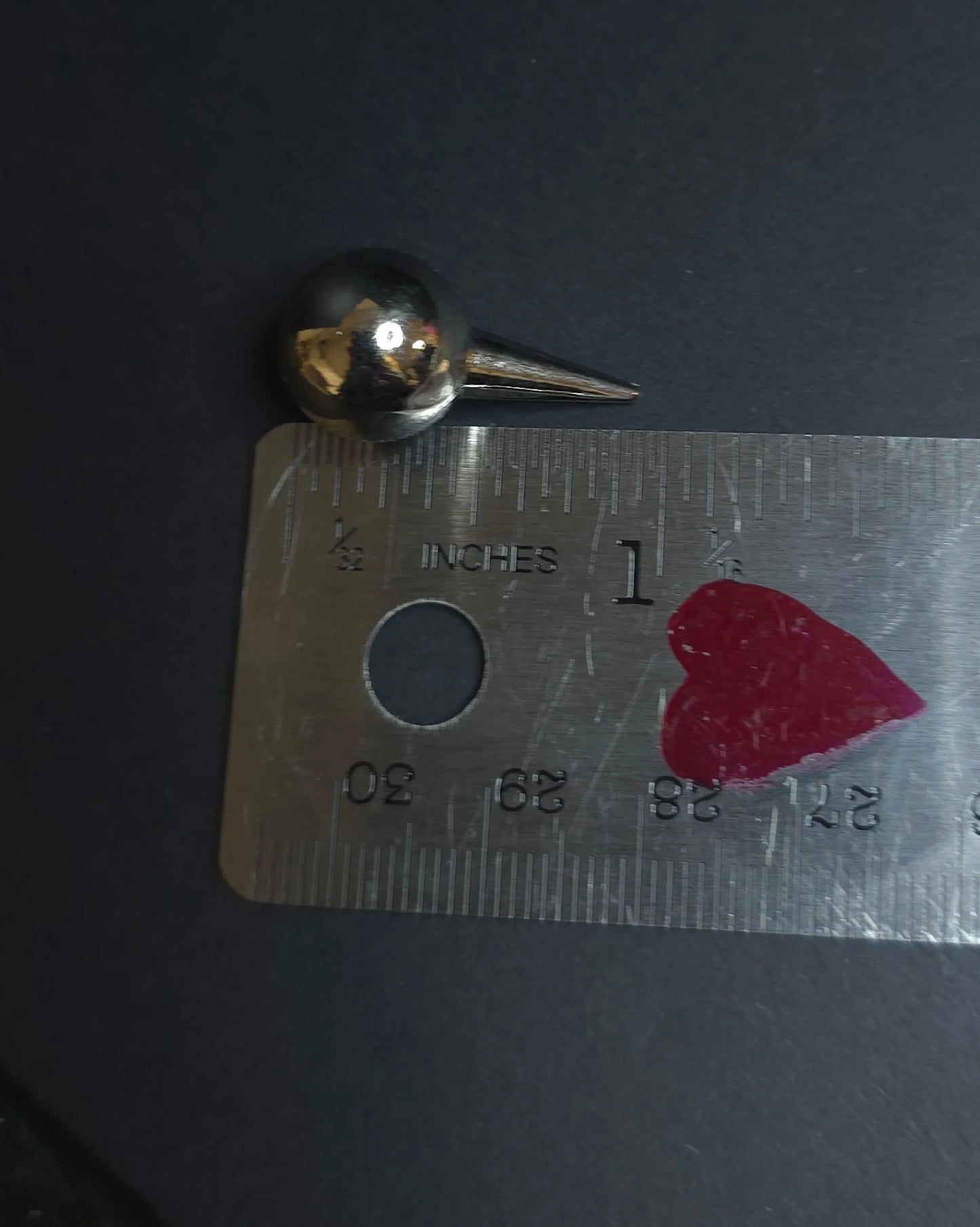 Small metal object on a ruler with a heart sticker against a dark background