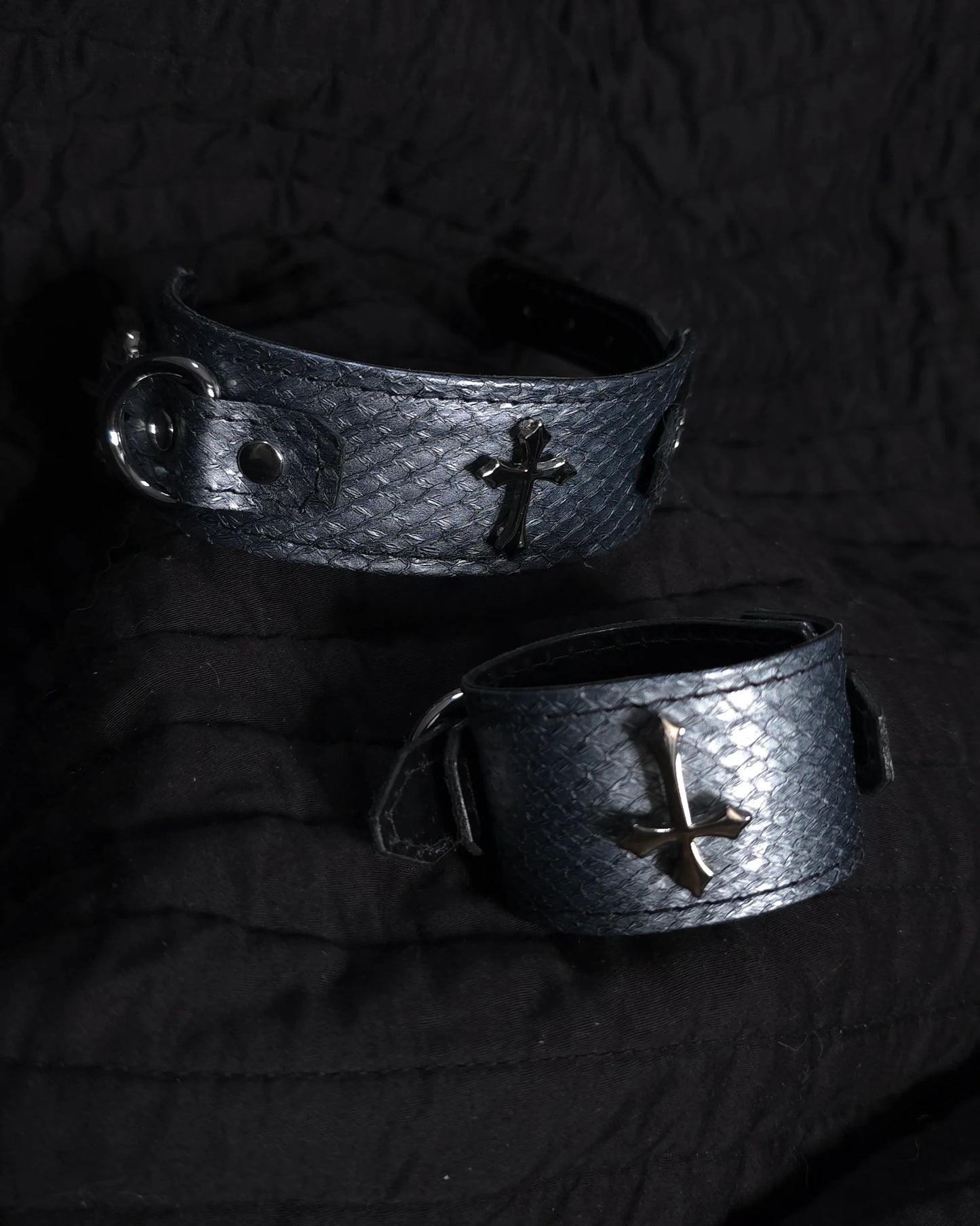 Two metallic bracelets with cross designs on a dark background