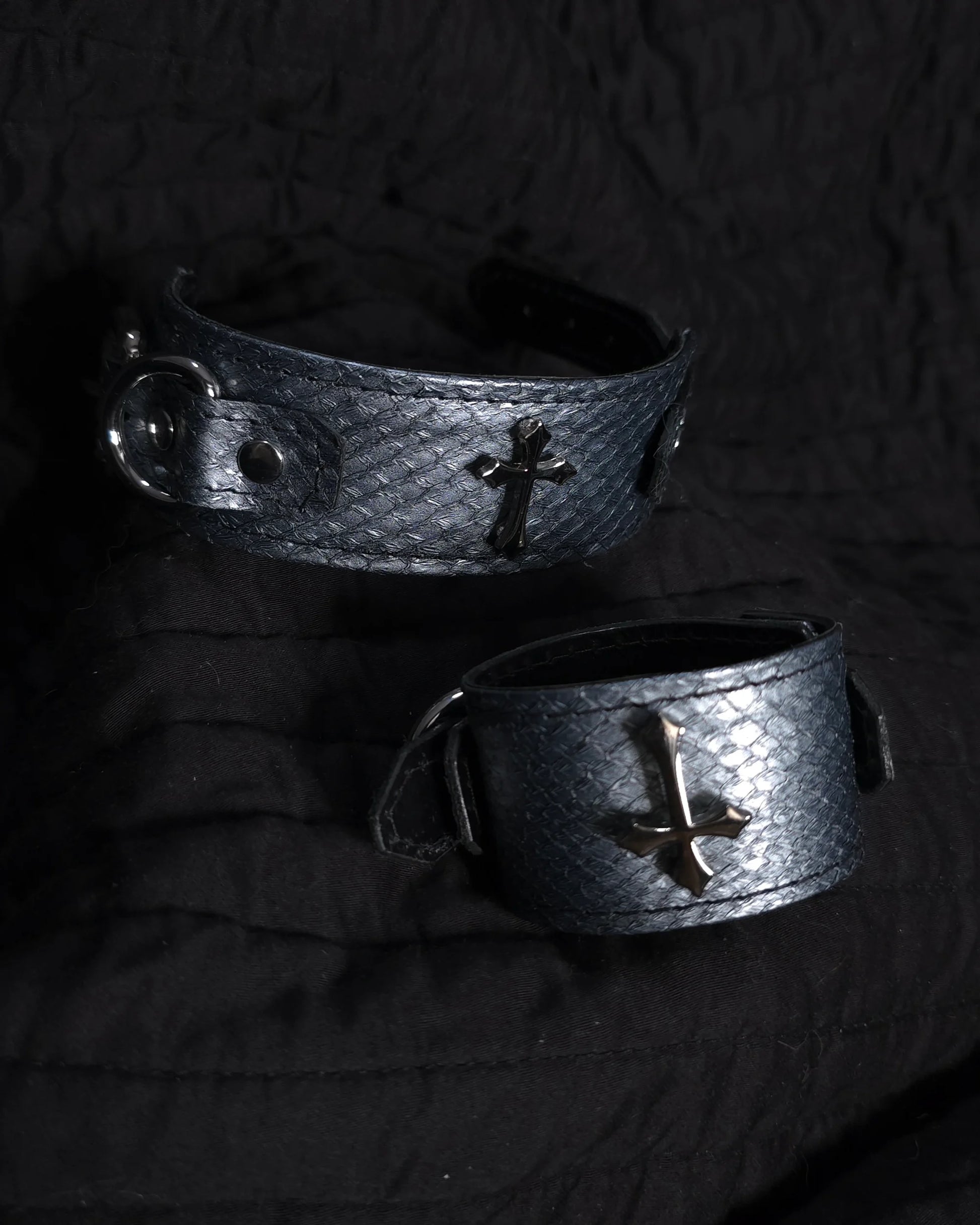 Two metallic bracelets with cross designs on a dark background