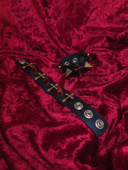 Black leather bracelet with gold accents on a red textured fabric background