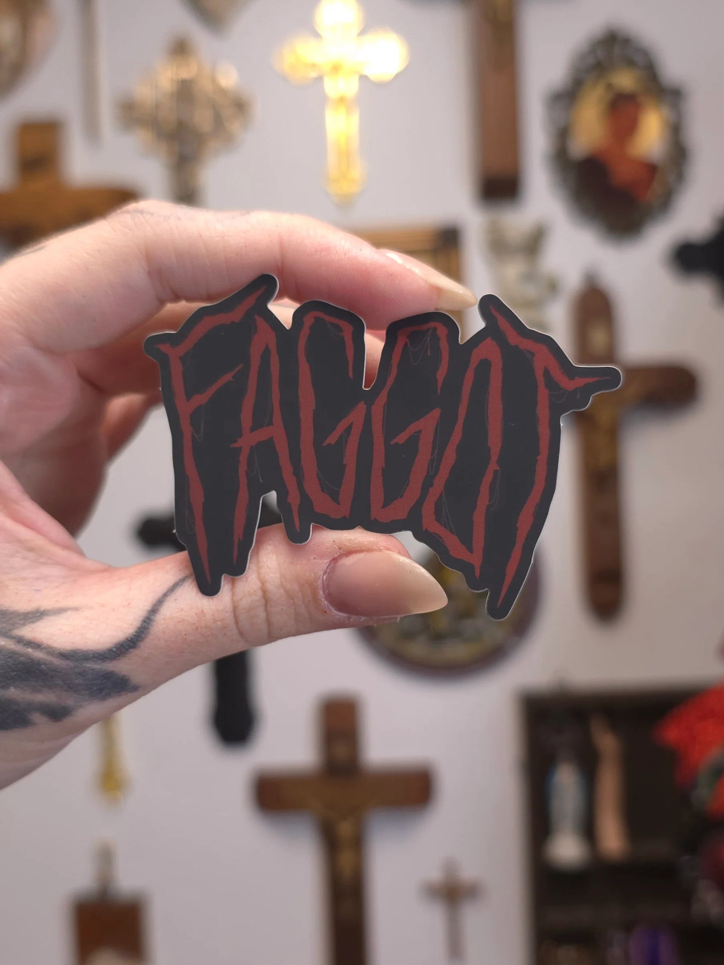 Hand holding a 'FAGGOT' sticker on blurry background