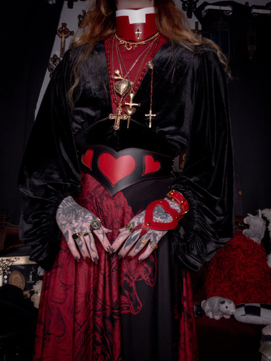 Person wearing a black and red outfit with heart designs and jewelry.