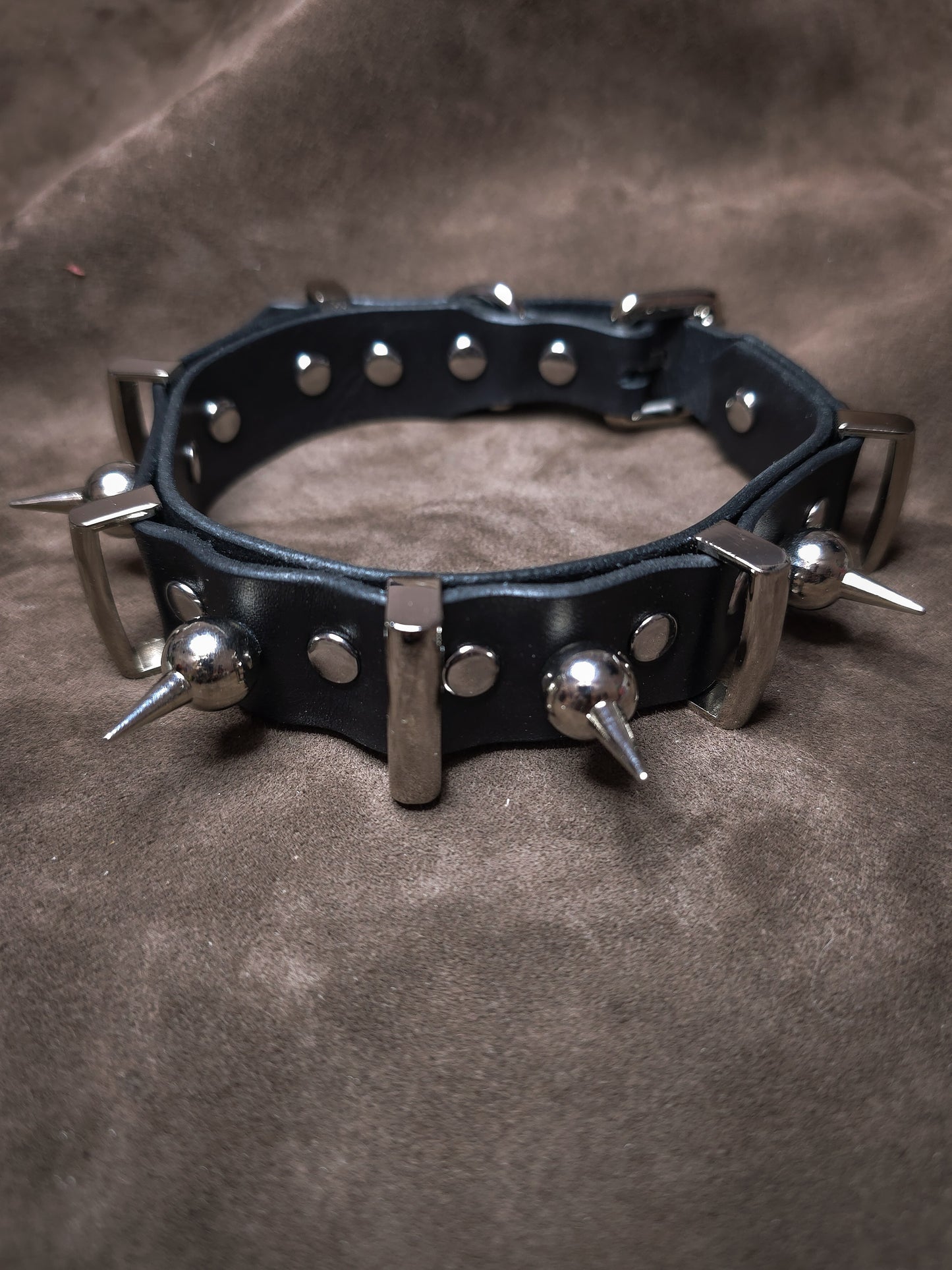 Black leather collar with metal spikes on a brown background