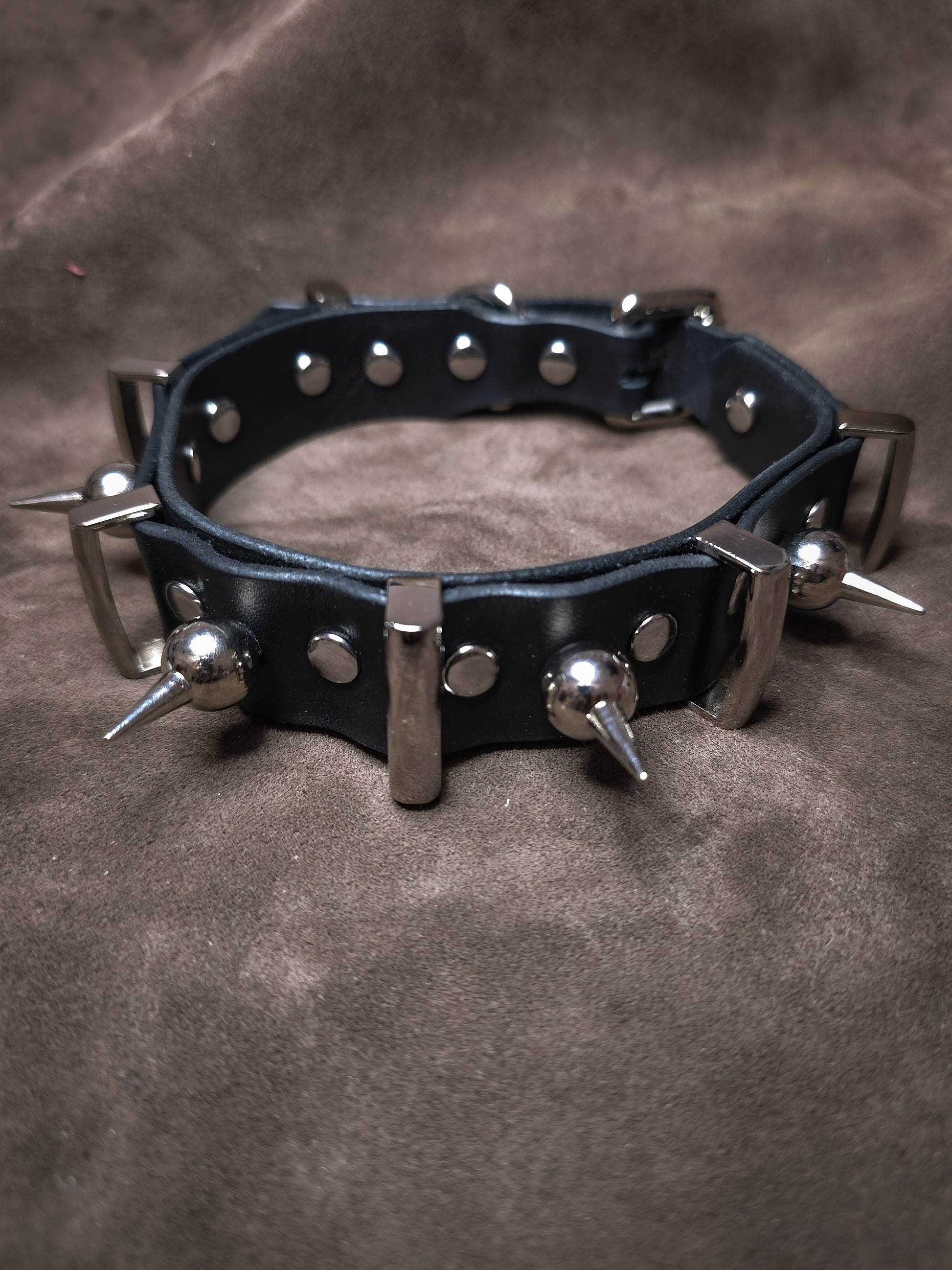 Black leather collar with metal spikes on a brown background