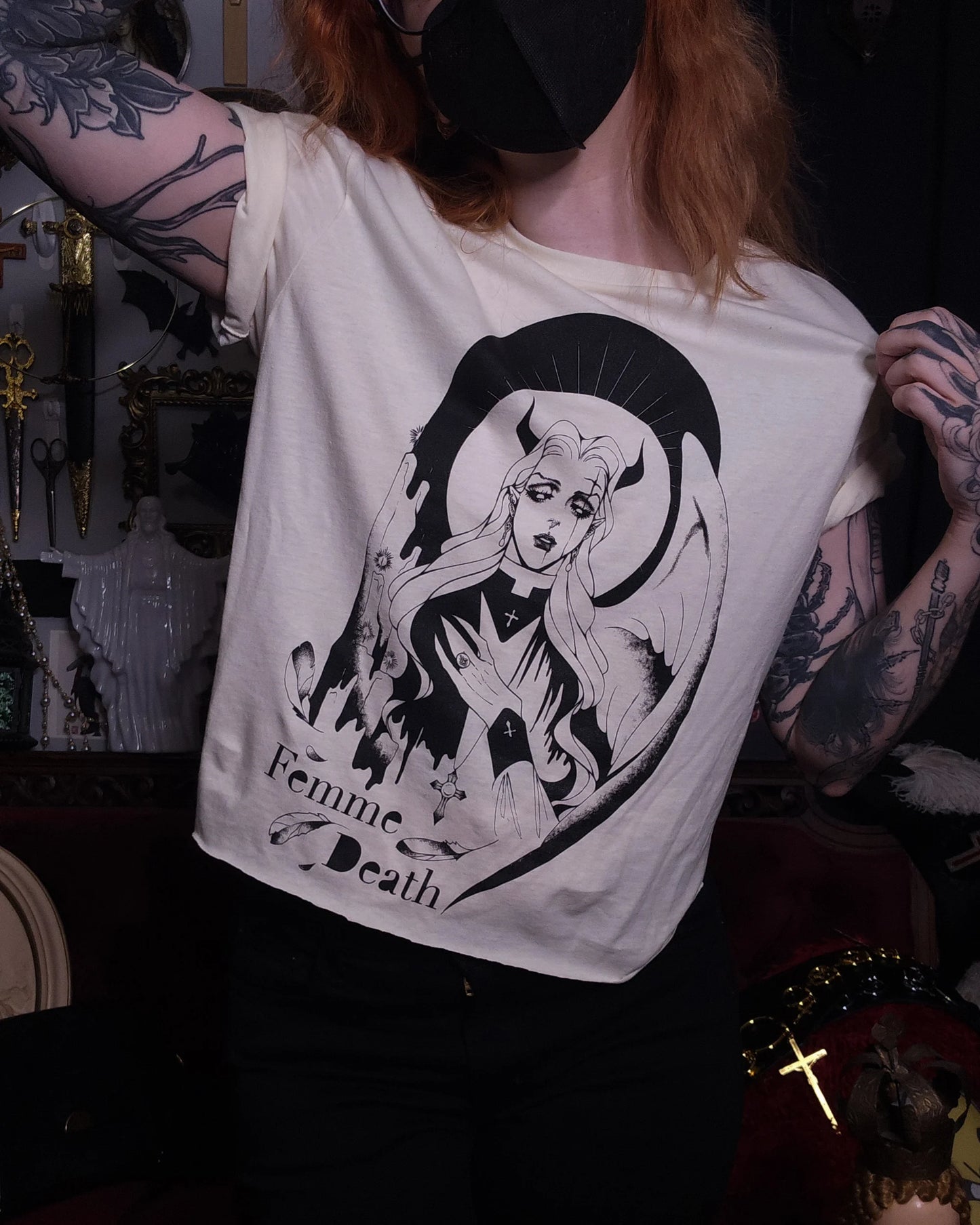 Person wearing a cream t-shirt with a black graphic design and text, set against a dark background.