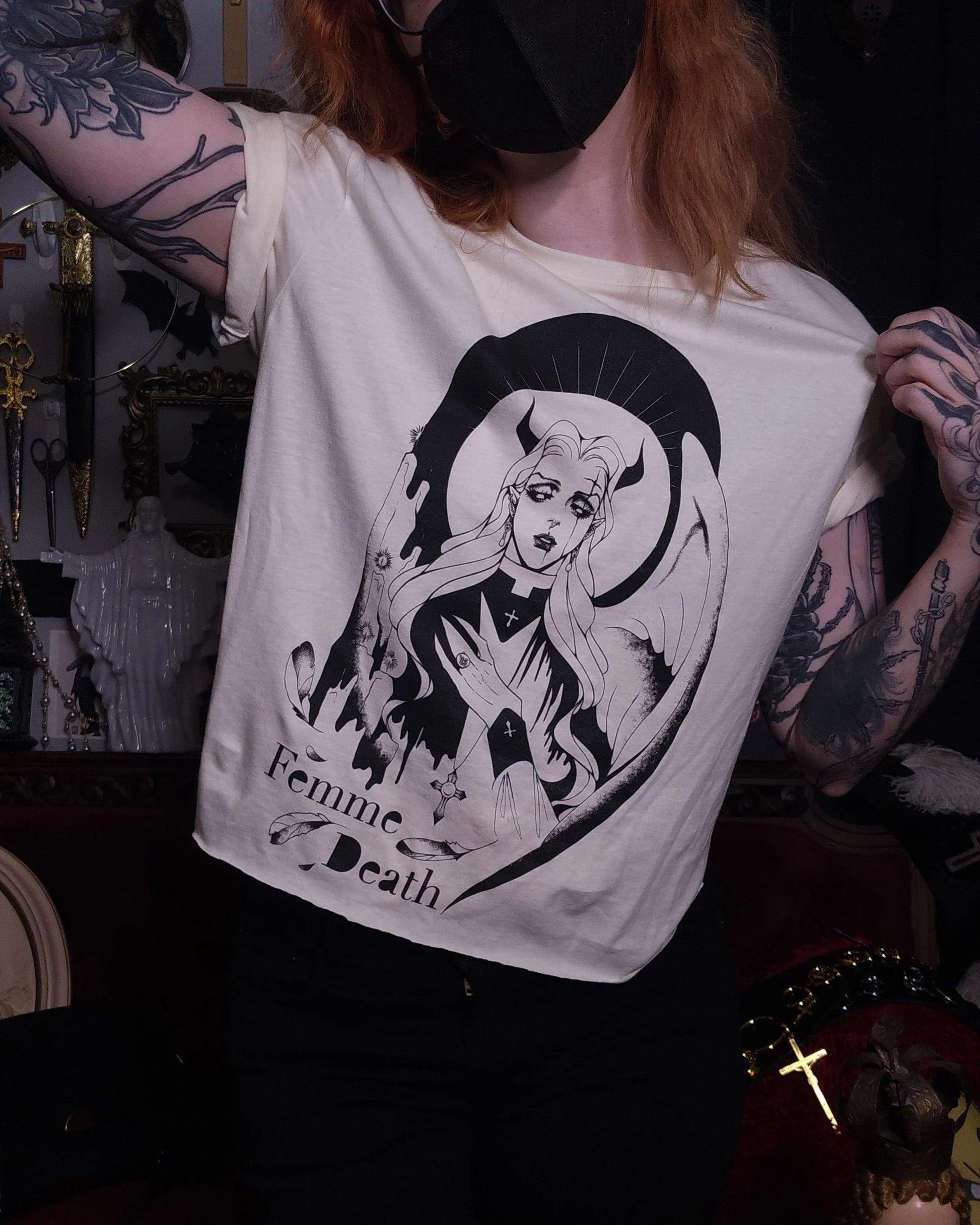 Person wearing a cream t-shirt with a black graphic design and text, set against a dark background.