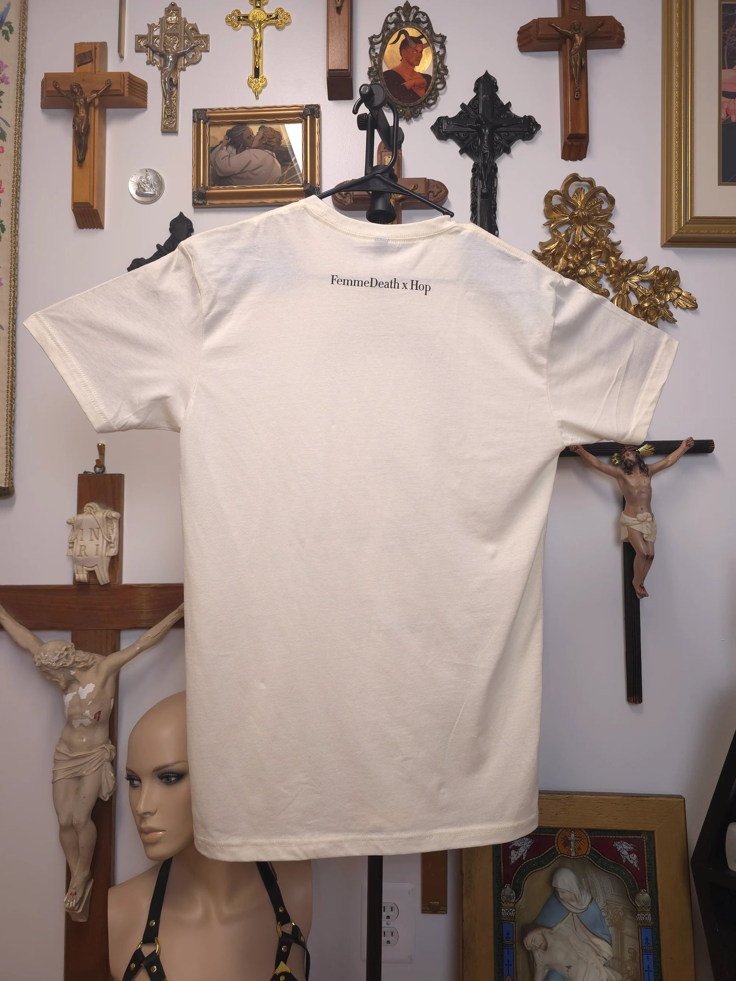 White t-shirt with text on a hanger in front of religious artwork