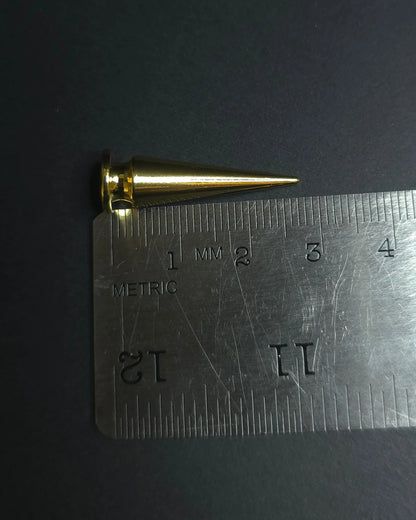 Gold cone-shaped spike next to a metal ruler on a dark background