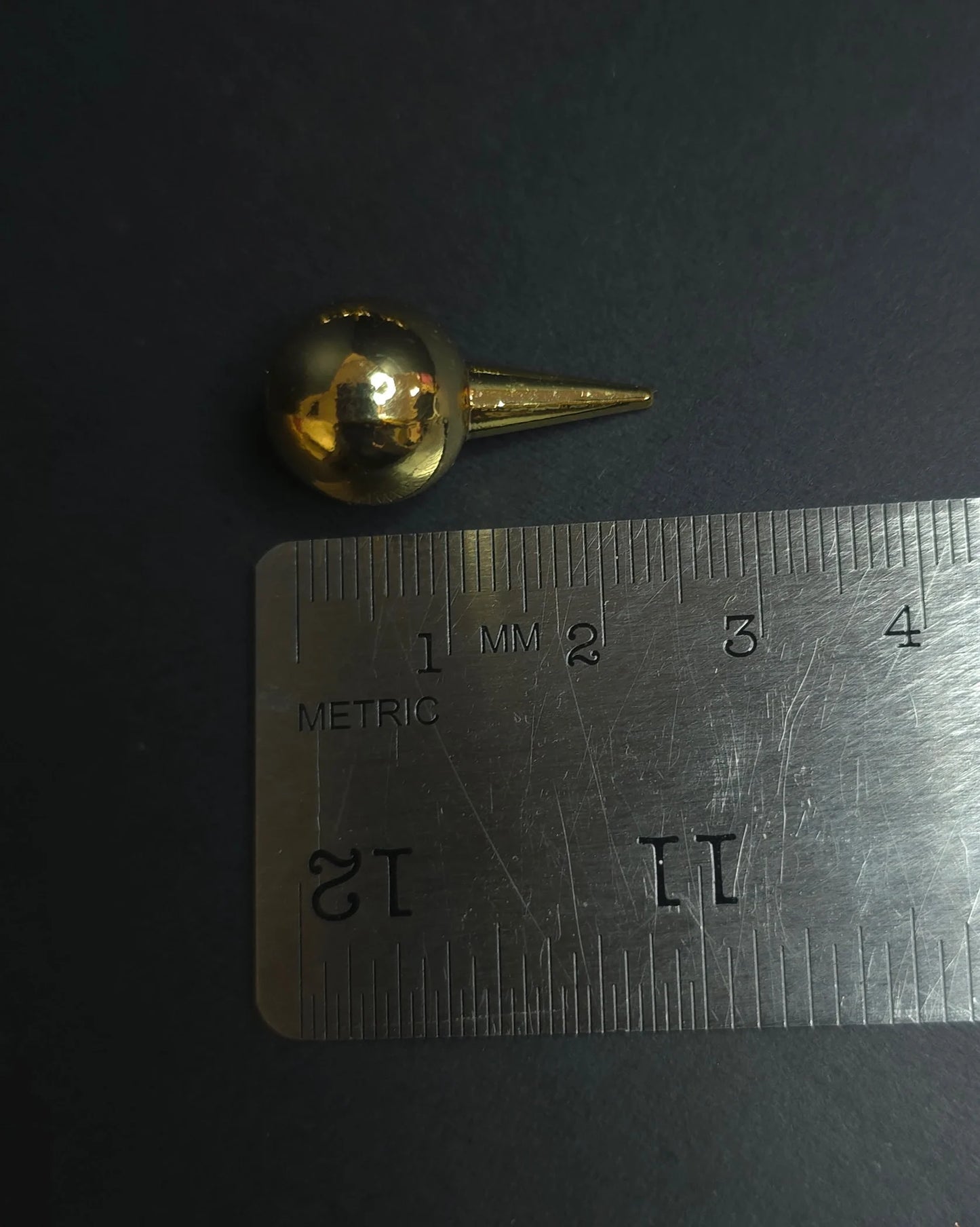 Gold spherical spike on a metallic ruler with measurements against a dark background