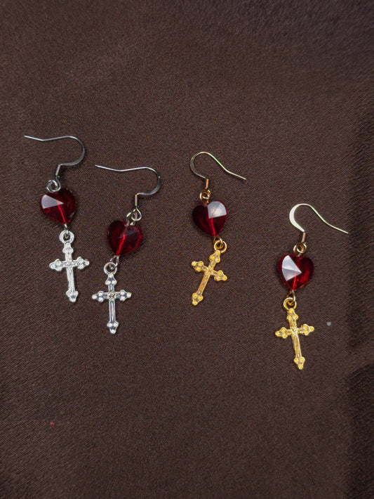 Two pairs of earrings with crosses and heart shaped beads on a brown background