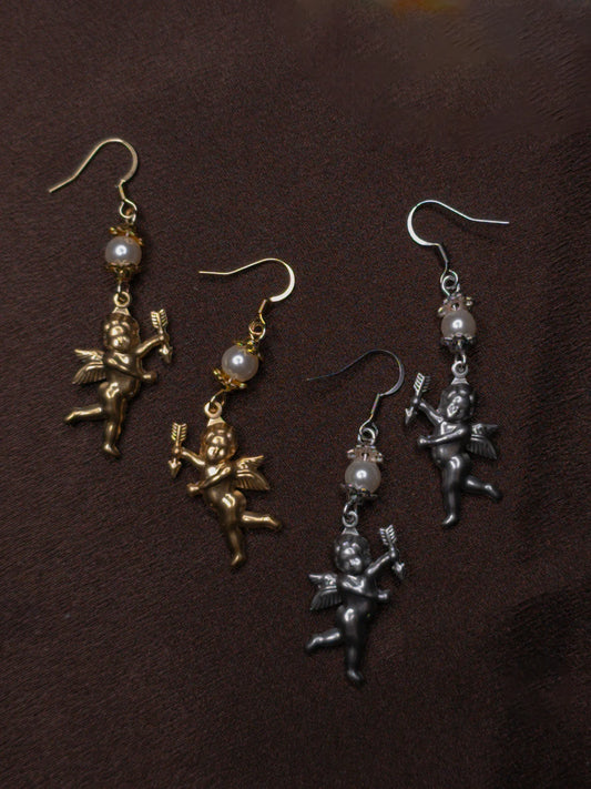 Two pairs of angel-shaped earrings in gold and silver on a dark brown background.