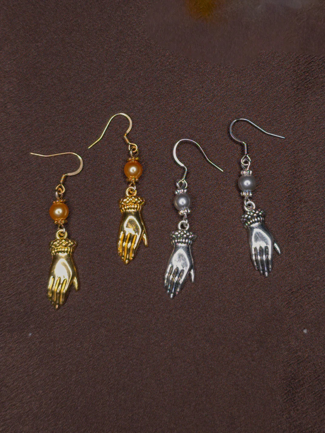 Two pairs of hand-shaped earrings on a brown background