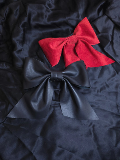 Two leather  bows, one red and one black, on black fabric background.