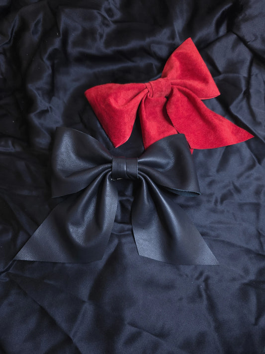 Two leather  bows, one red and one black, on black fabric background.