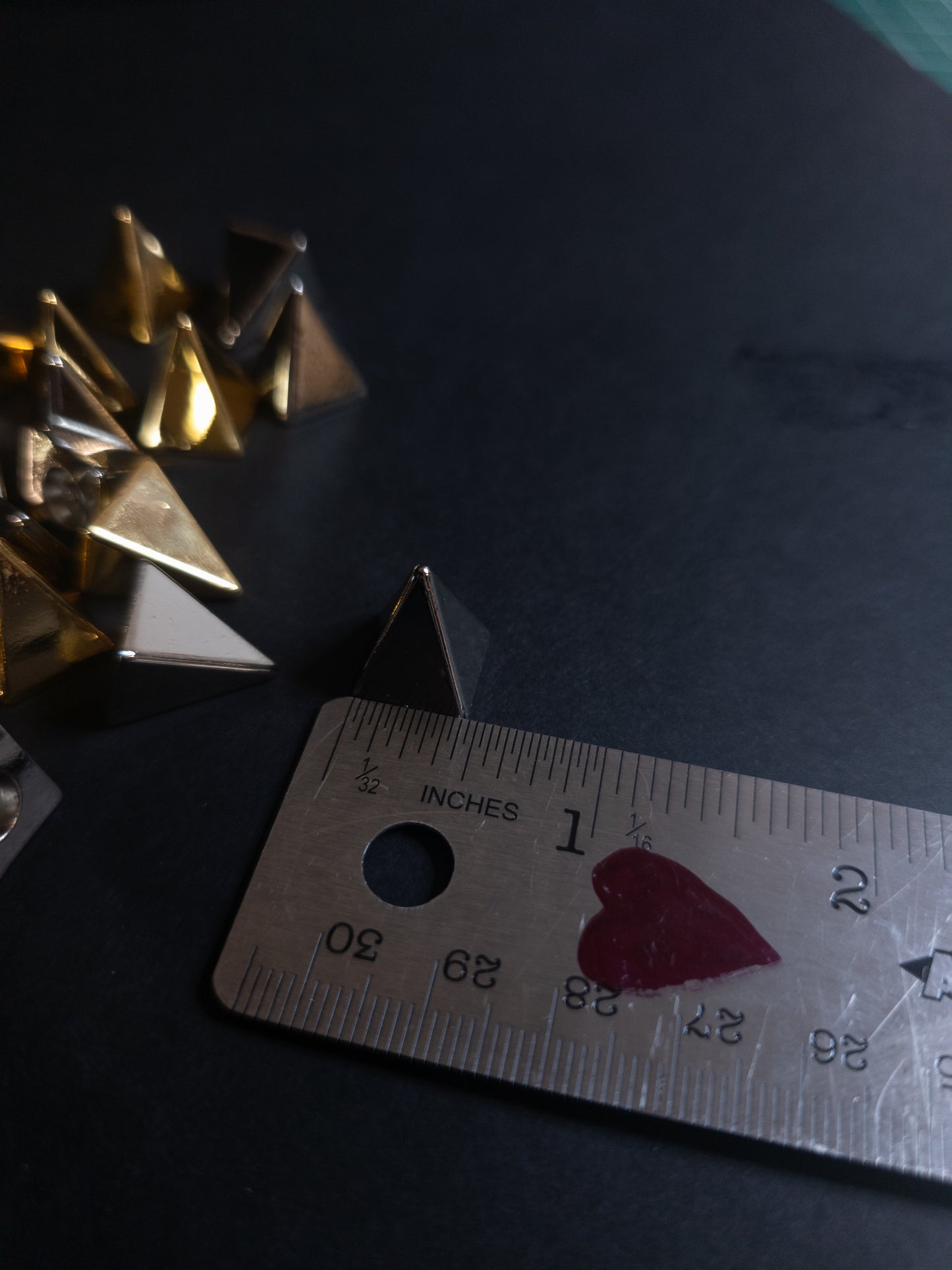 Metallic pyramid spike next to a ruler on a dark surface