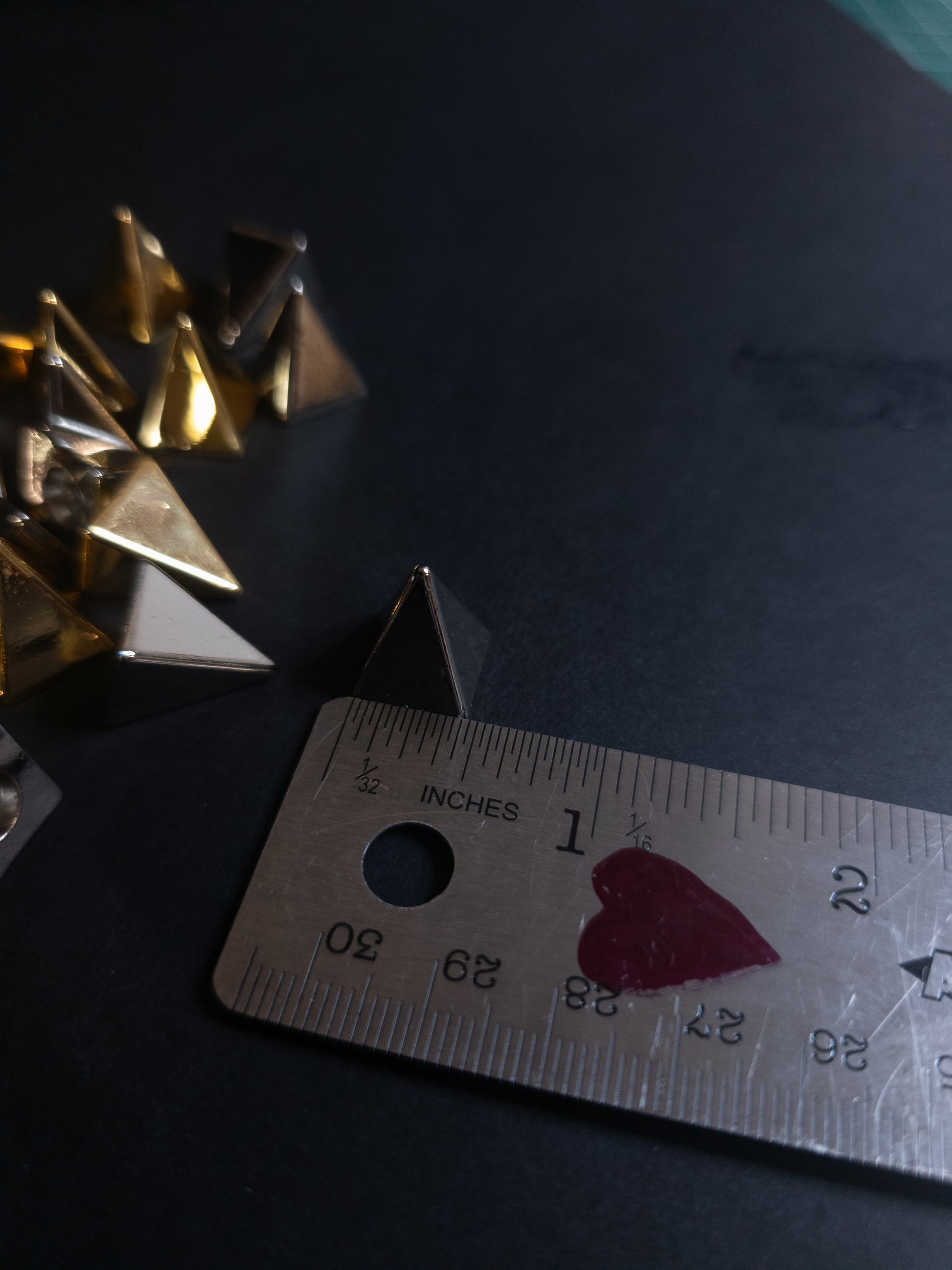 Metallic pyramid spike next to a ruler on a dark surface