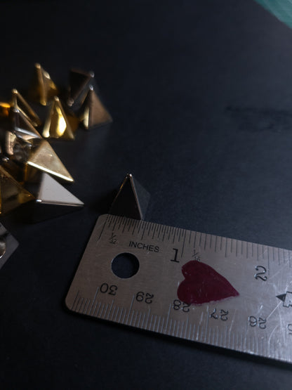 Metallic pyramid spike next to a ruler on a dark surface