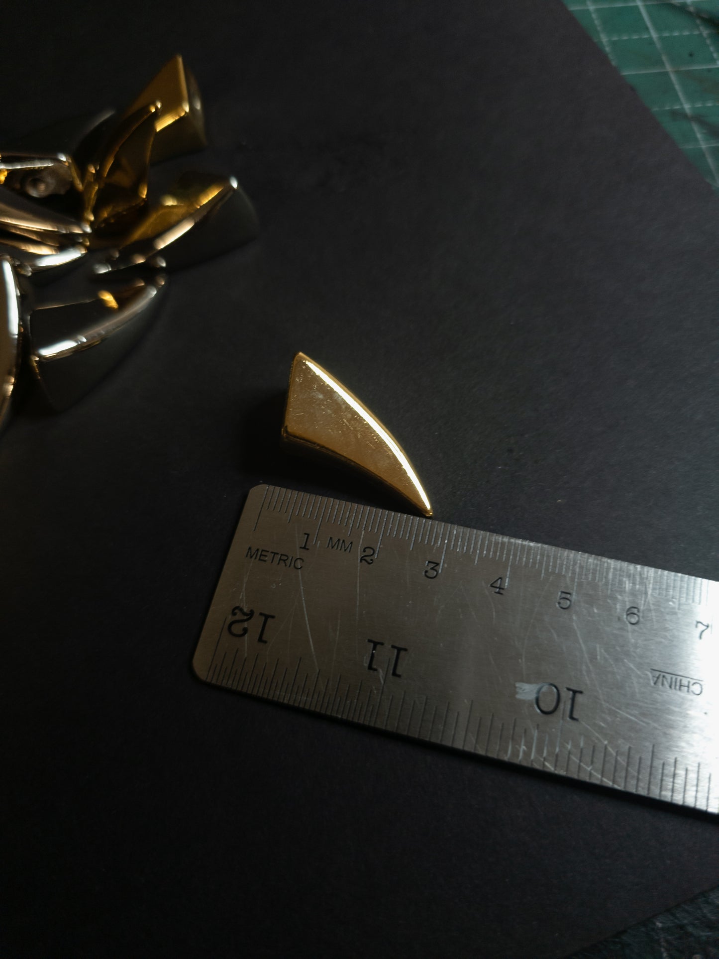Gold decorative item next to a ruler on a dark surface