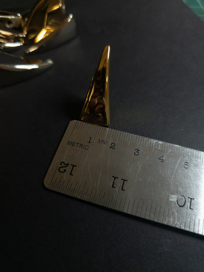 Gold decorative object next to a metal ruler on a dark surface