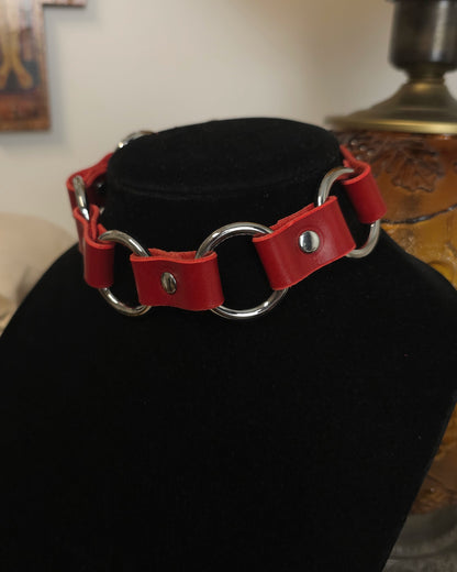 Red leather collar with silver hardware on a black stand.