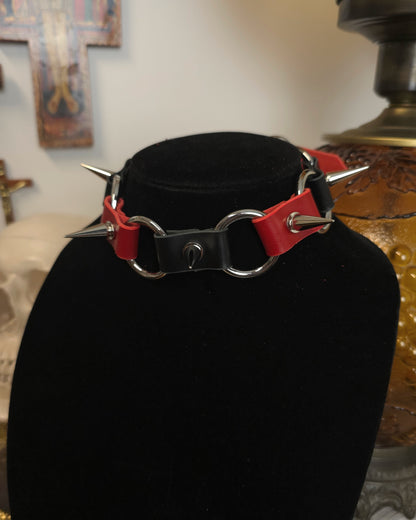 Black choker with red accents and spikes on a black stand against a blurred background