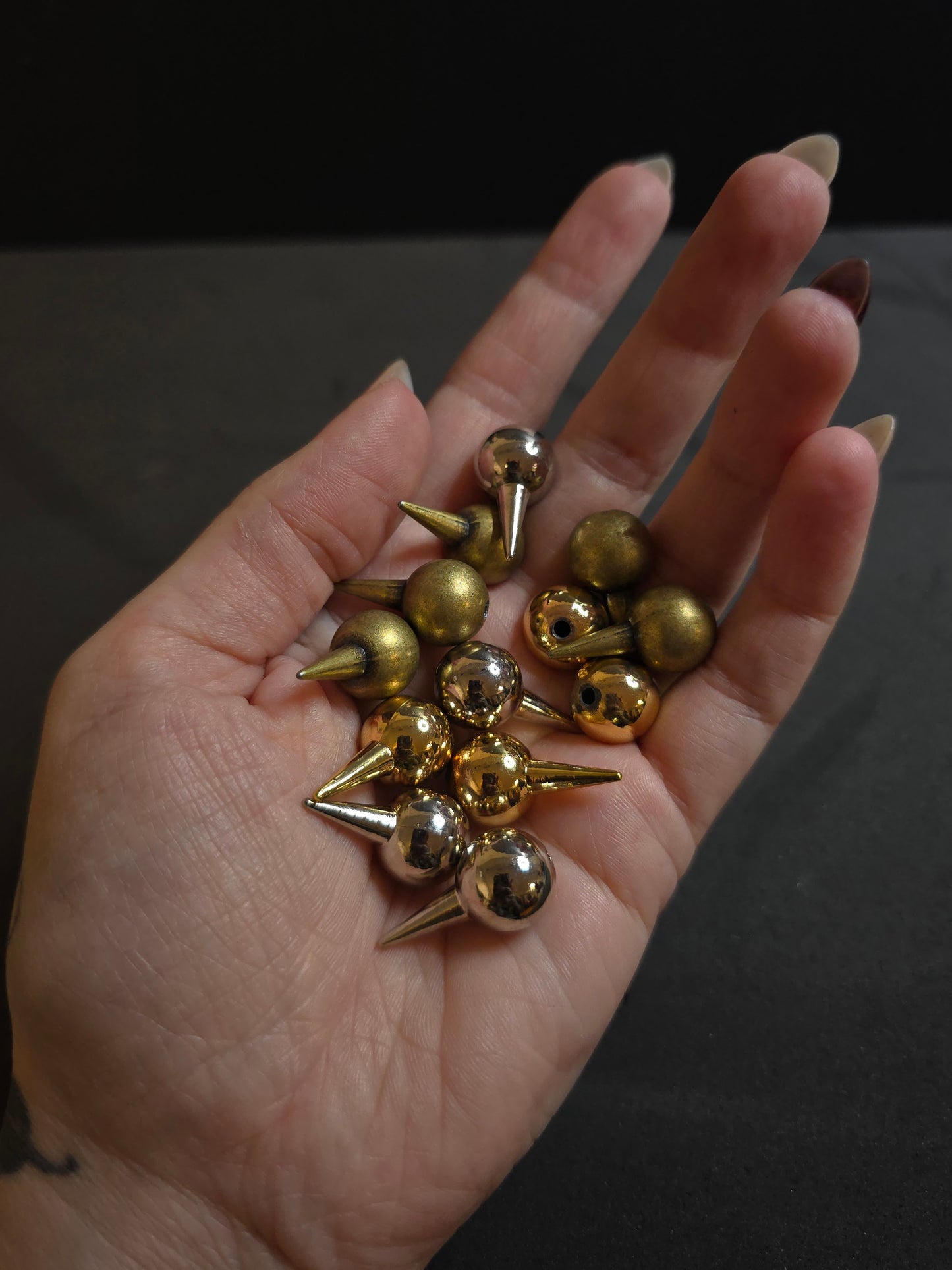 hand holding silver, golden, and bronze spikes on black background
