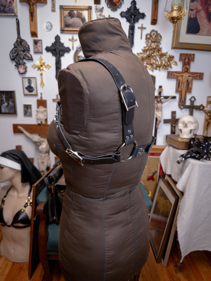 side back view of black leather harness with crosses on a brown fabric mannequin against a gothic background