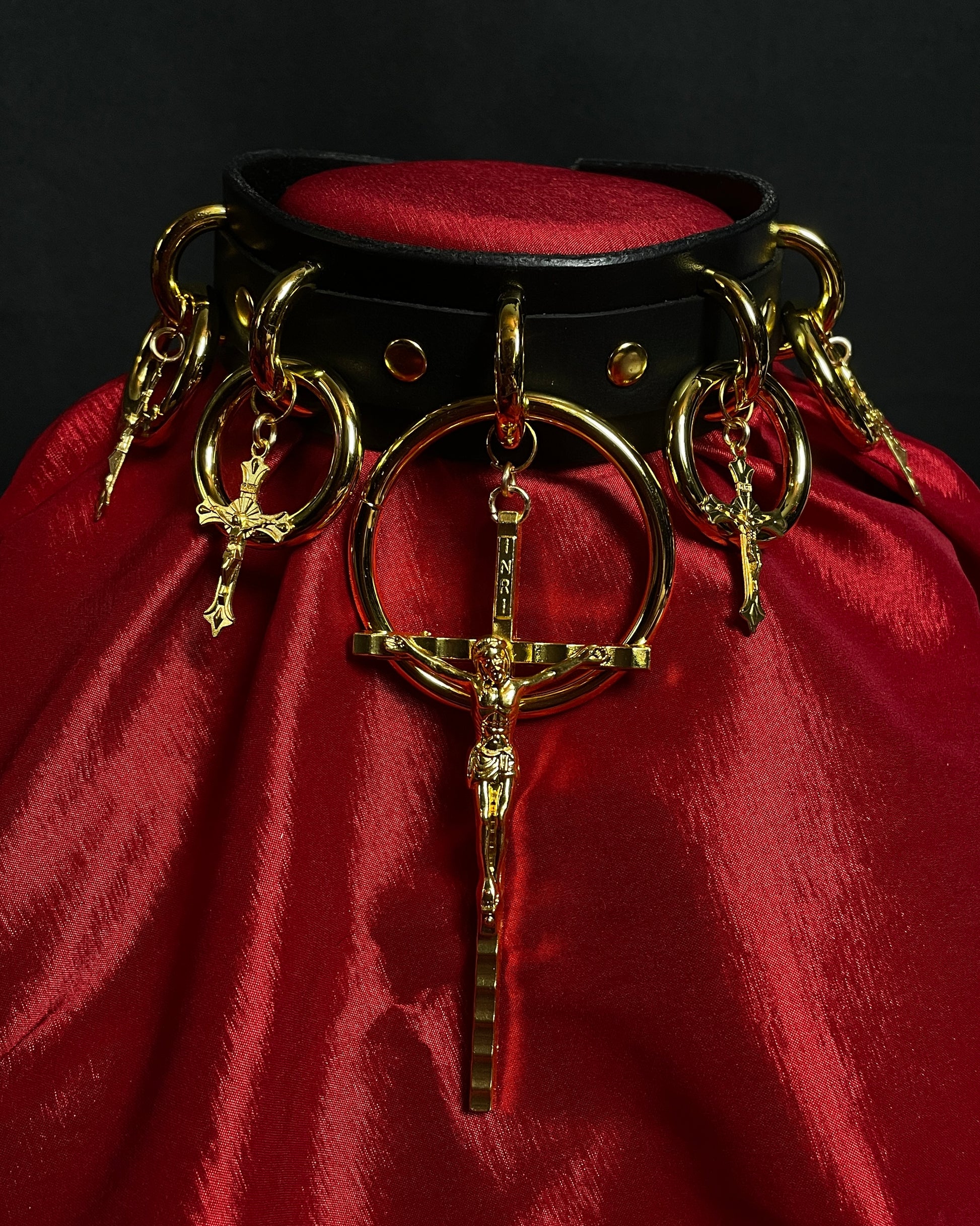 Decorative collar with gold rings and cross pendant on a red fabric background