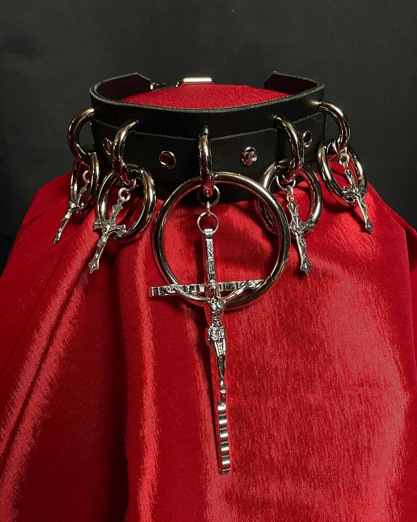 Black leather collar with metal rings and crosses on a red fabric background