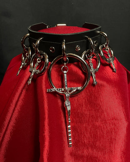 Black leather collar with metal rings and crosses on a red fabric background