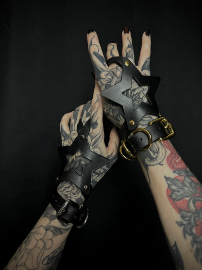 Tattooed hands wearing black leather gloves with star designs on a dark background