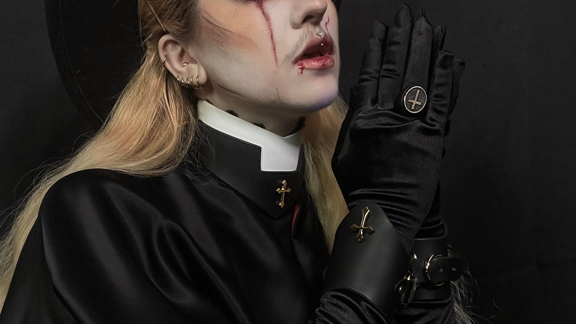 Image features a portrait of a person from the nose to shoulders wearing leather priest collar and leather wrist cuffs.