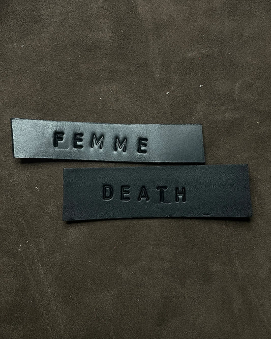 Two black leather patches with 'FEMME' and 'DEATH' text on a dark brown background.