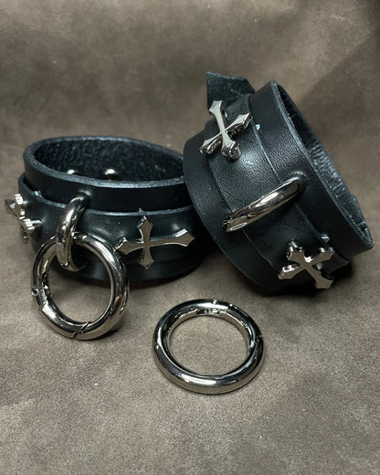 Black leather cuffs with silver rings and crosses on a gray background
