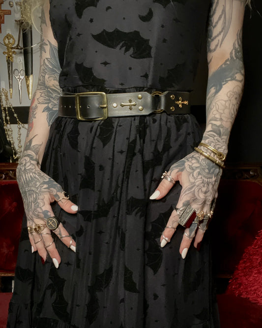 Person wearing a black dress with gold belt and tattoos on arms and hands.