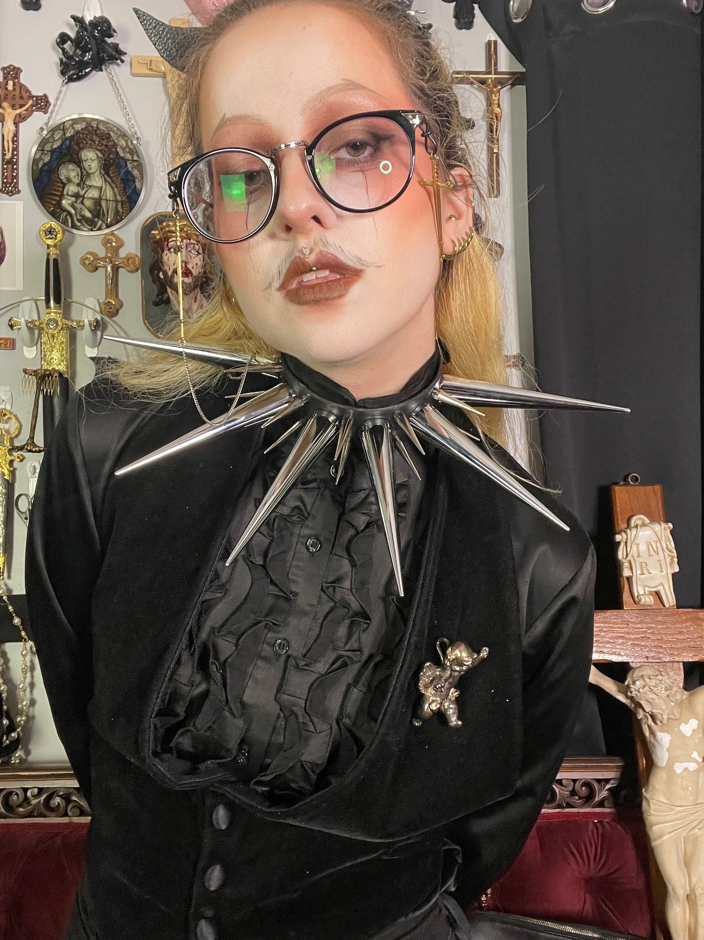 Person with blond hair and glasses wearing all black and oversized spiked collar
