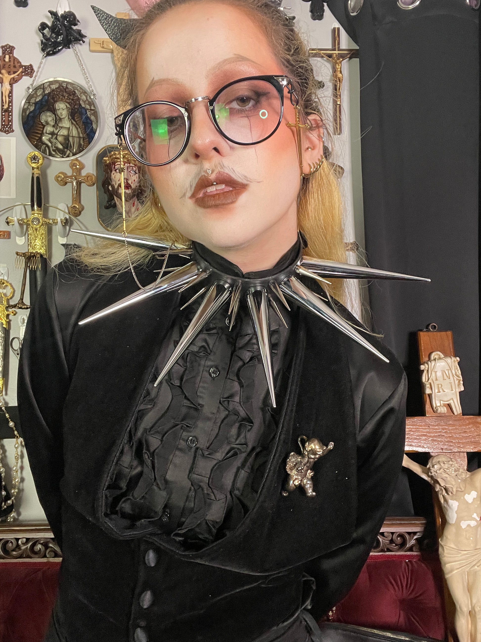 Person with blond hair and glasses wearing all black and oversized spiked collar