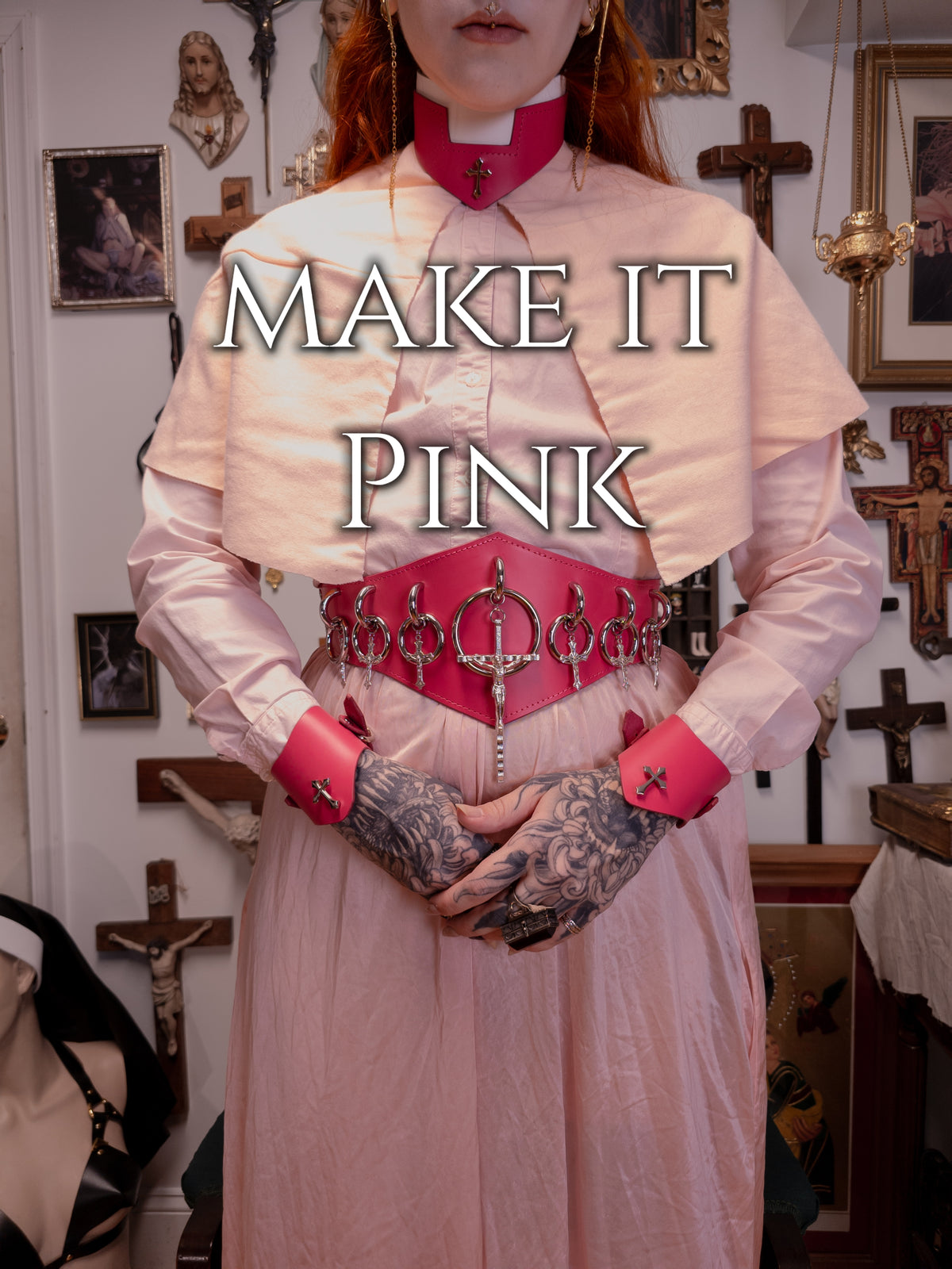 Person dressed in pink priest outfit with pink leather accessories on a gothic background, with the words "make it pink"