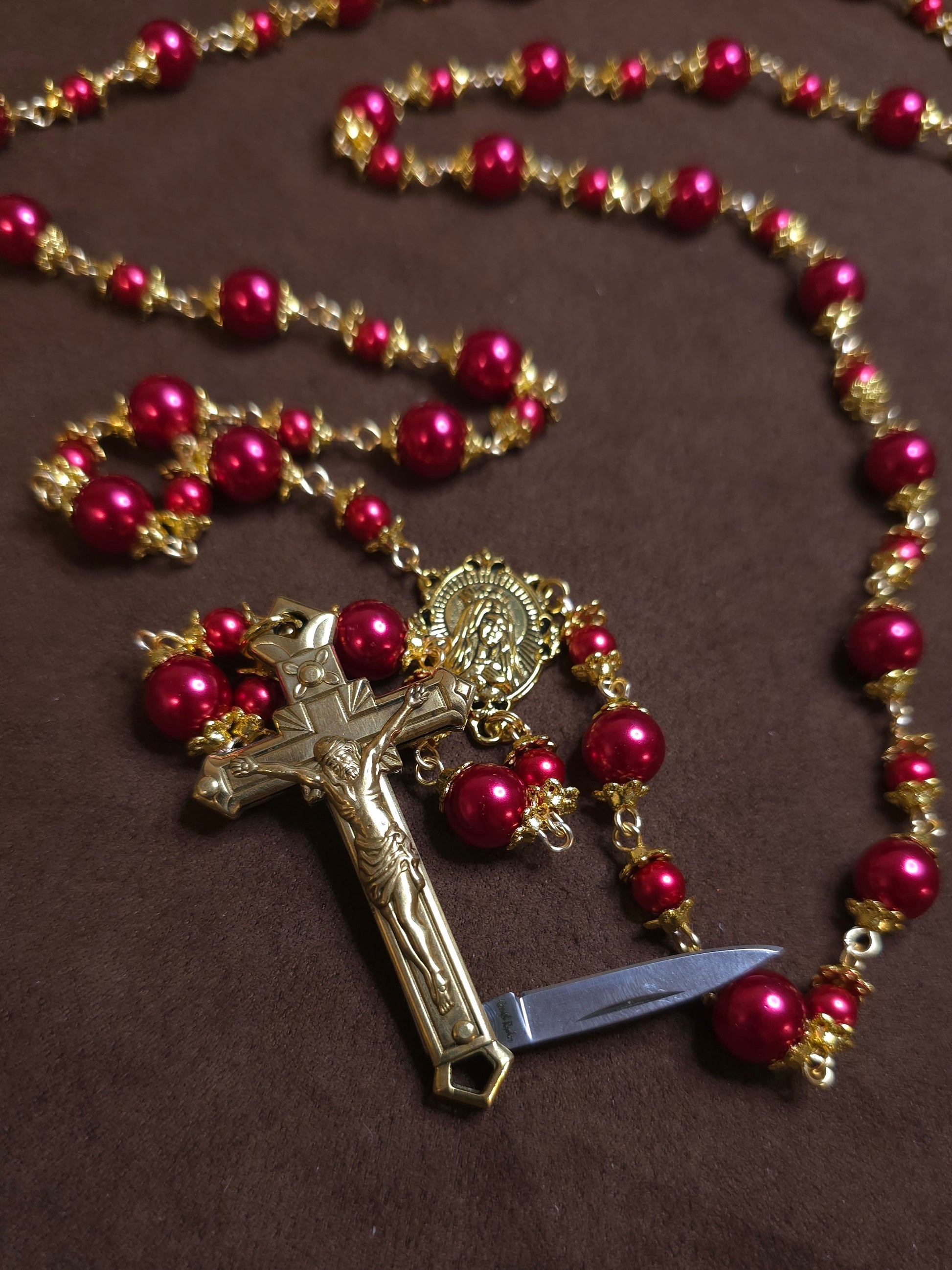 Rosary with red beads and a gold cross on a brown background
