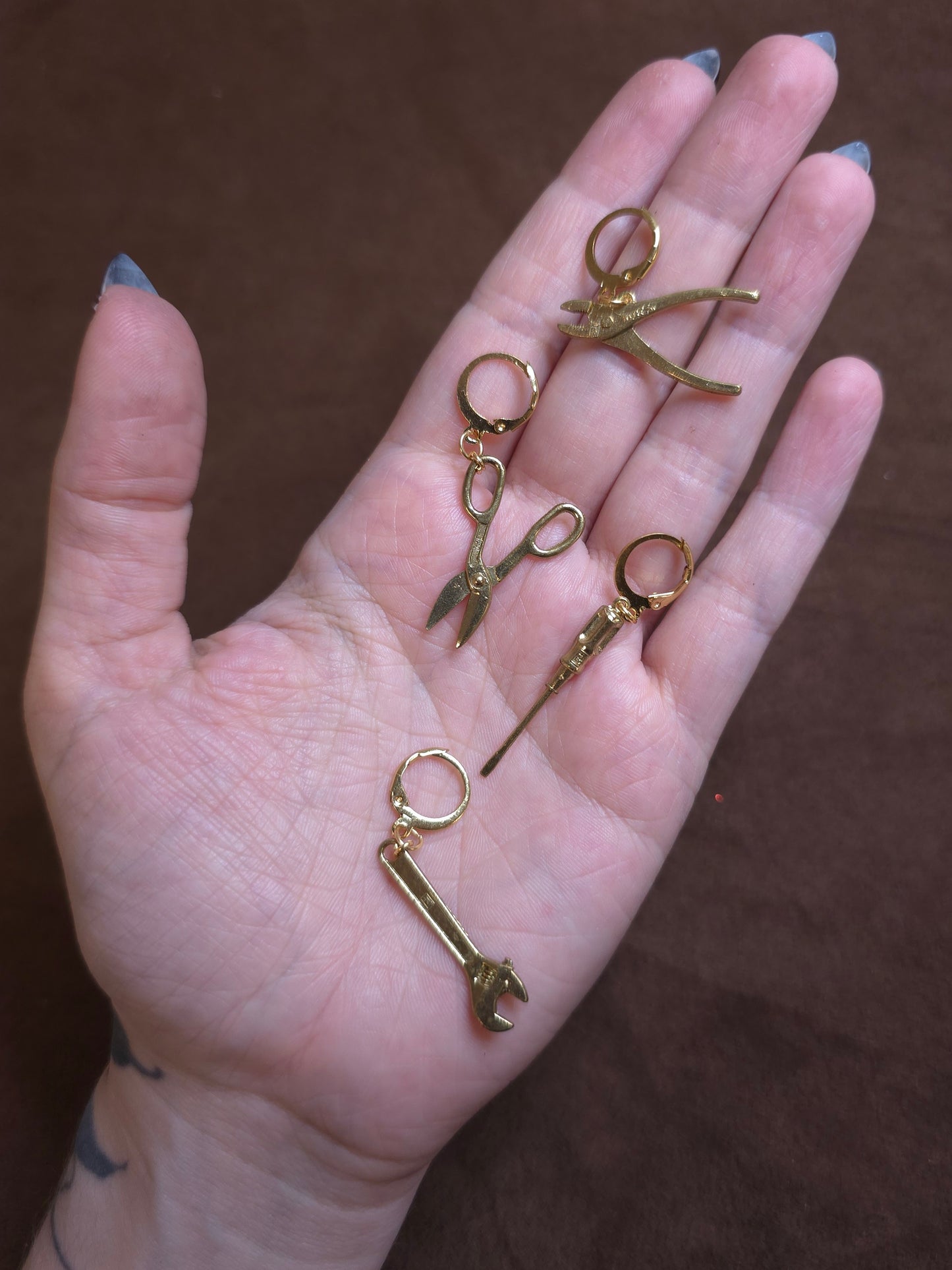 Hand holding small gold jewelry pieces against a brown background