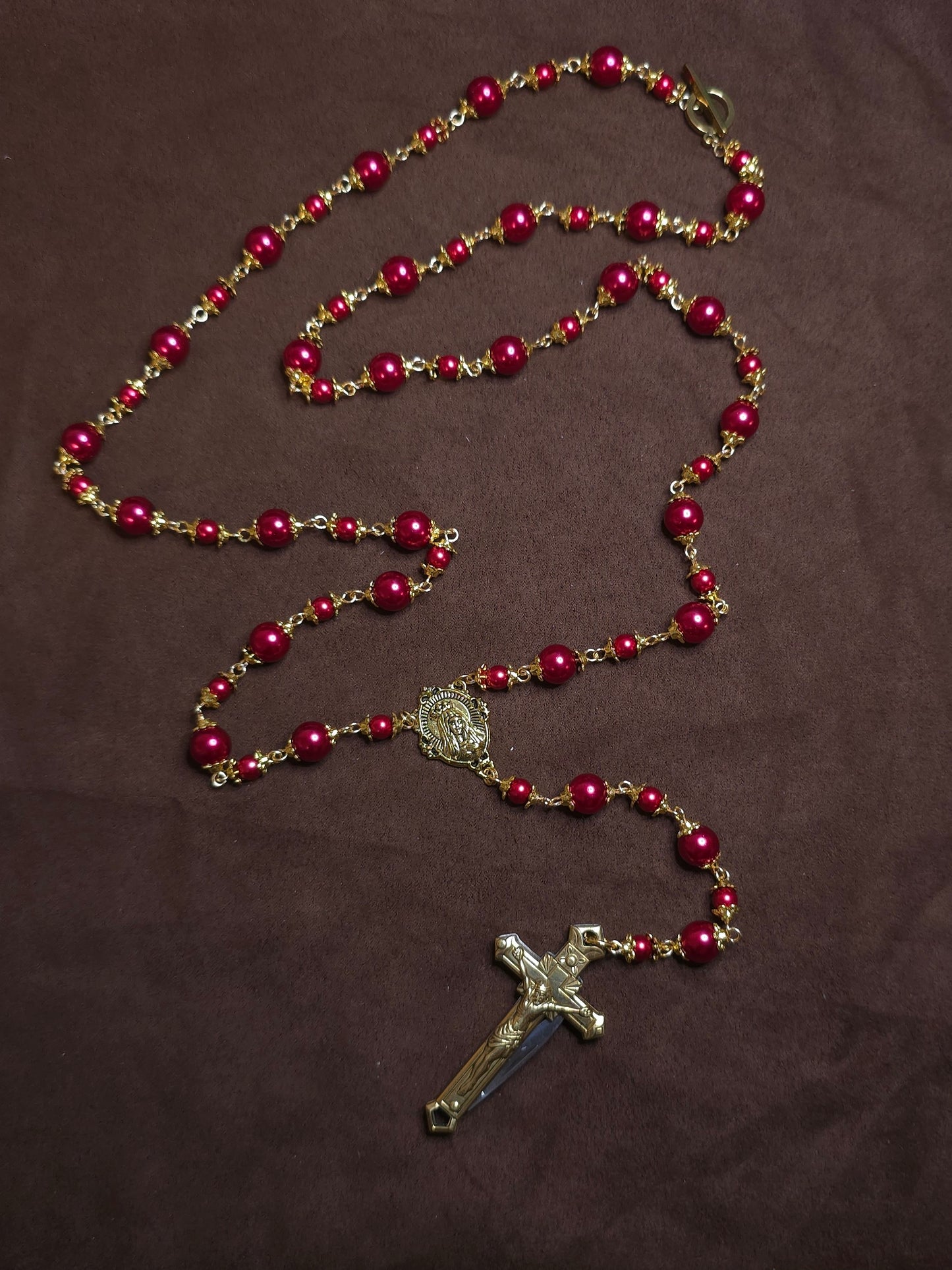 Red beaded rosary with a cross on a brown background